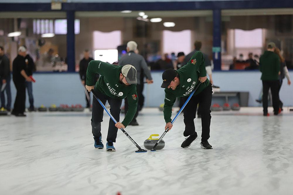 Two men in OAC gear curling.