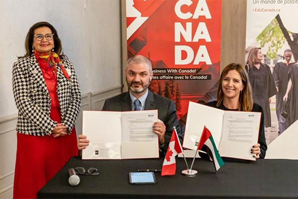 three people at a table, two holding signed documents for the camera