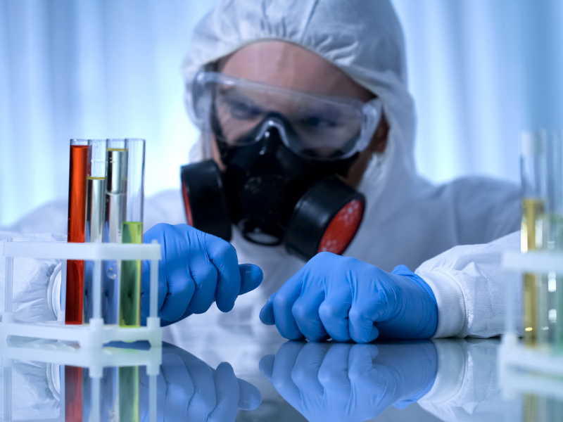  A student in a lab coat and mask conducting an experiment with a test tube.