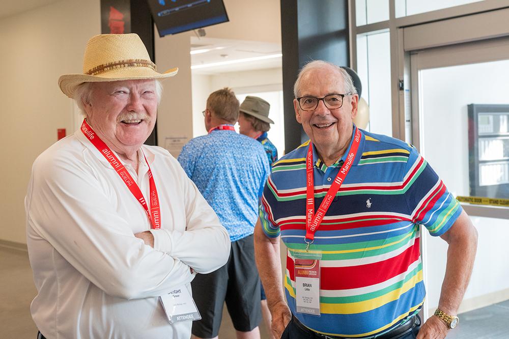 Two older men standing together and smiling.