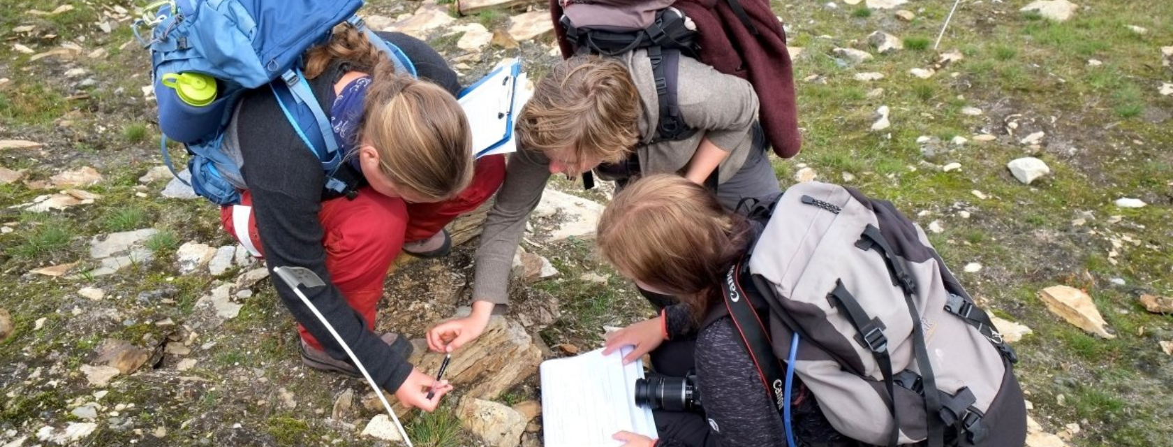 Three student researchers with backpacks studying a map on a trail.