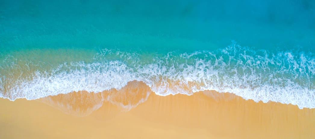 Blue ocean water meeting the sand with a small wave