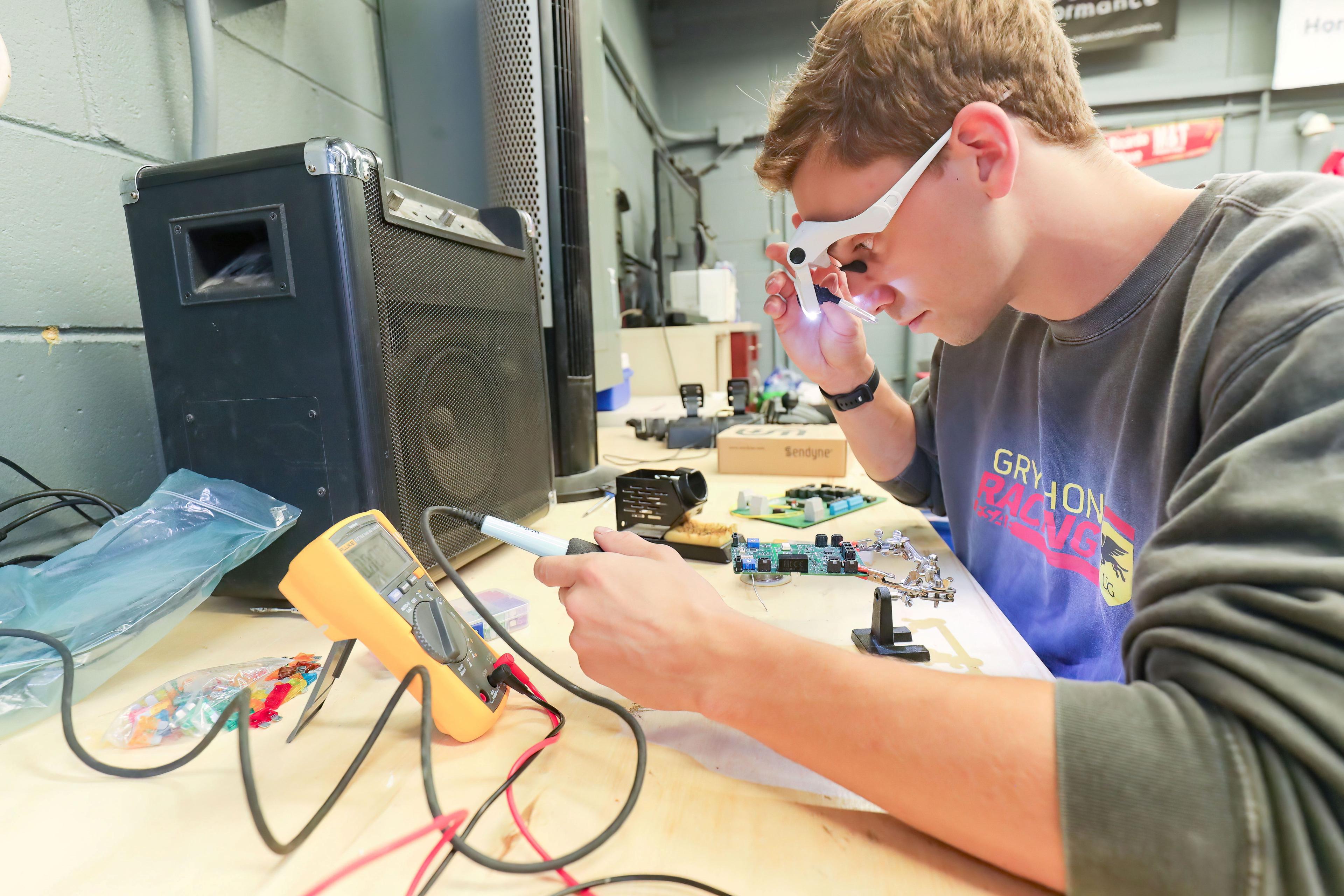 Engineering student in a lab with goggles on using a piece of equipment.