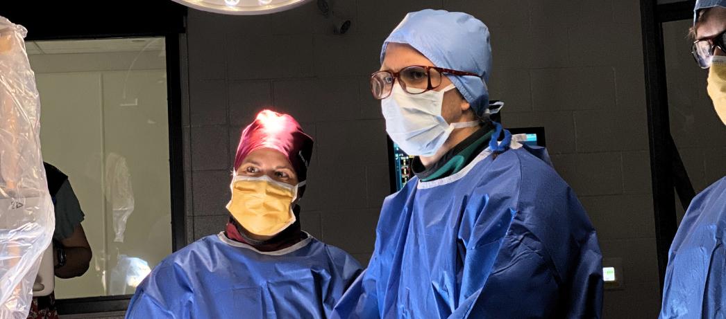 Two surgeons wearing caps, masks, glasses and blue surgical gowns in an operating room