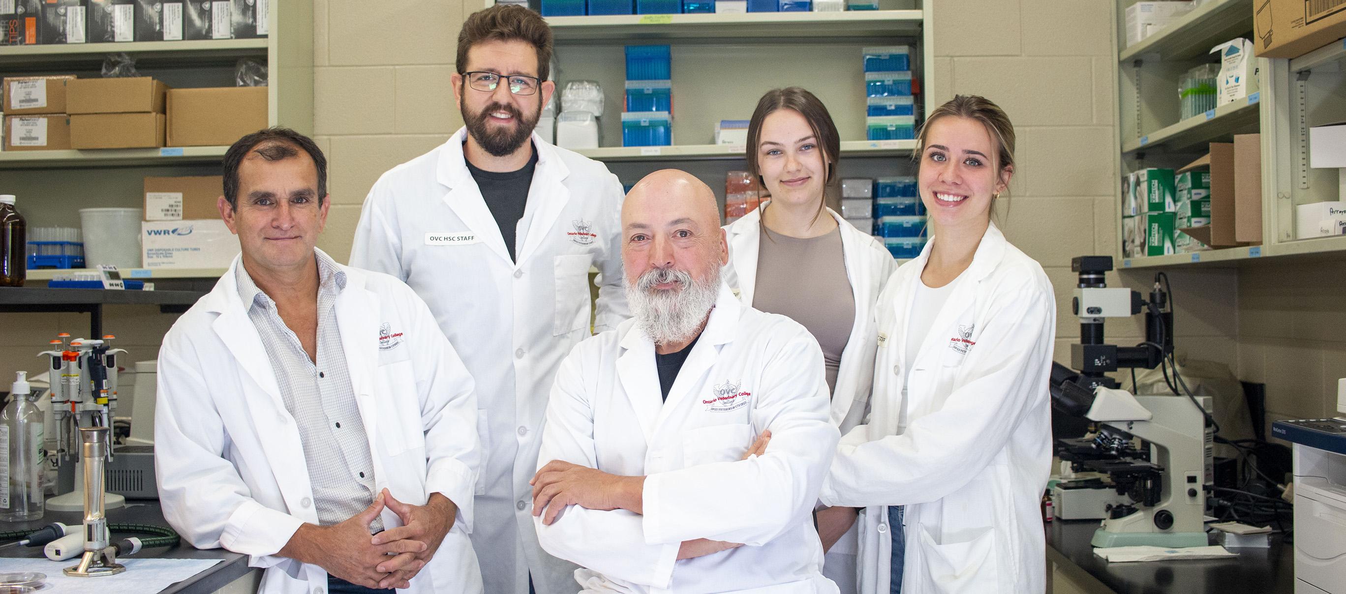 Dr. Mario Monteiro and team stand in lab together while wearing PPE