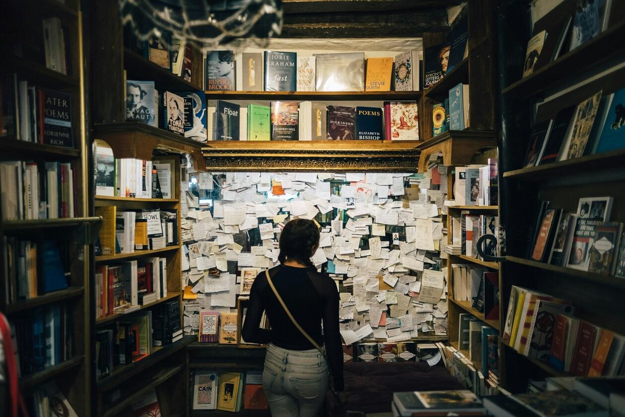 A woman stands before a bookshelf filled with numerous old books, showcasing her love for literature and history.