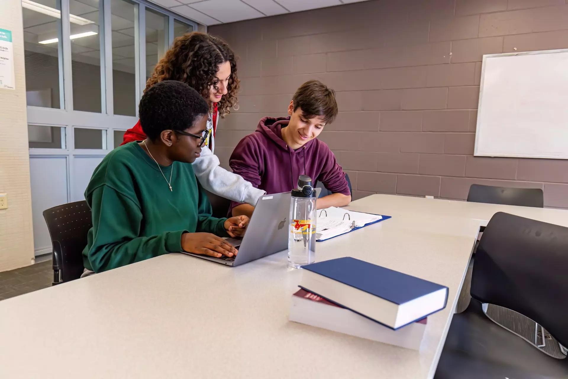3 students looking at a book in a study space