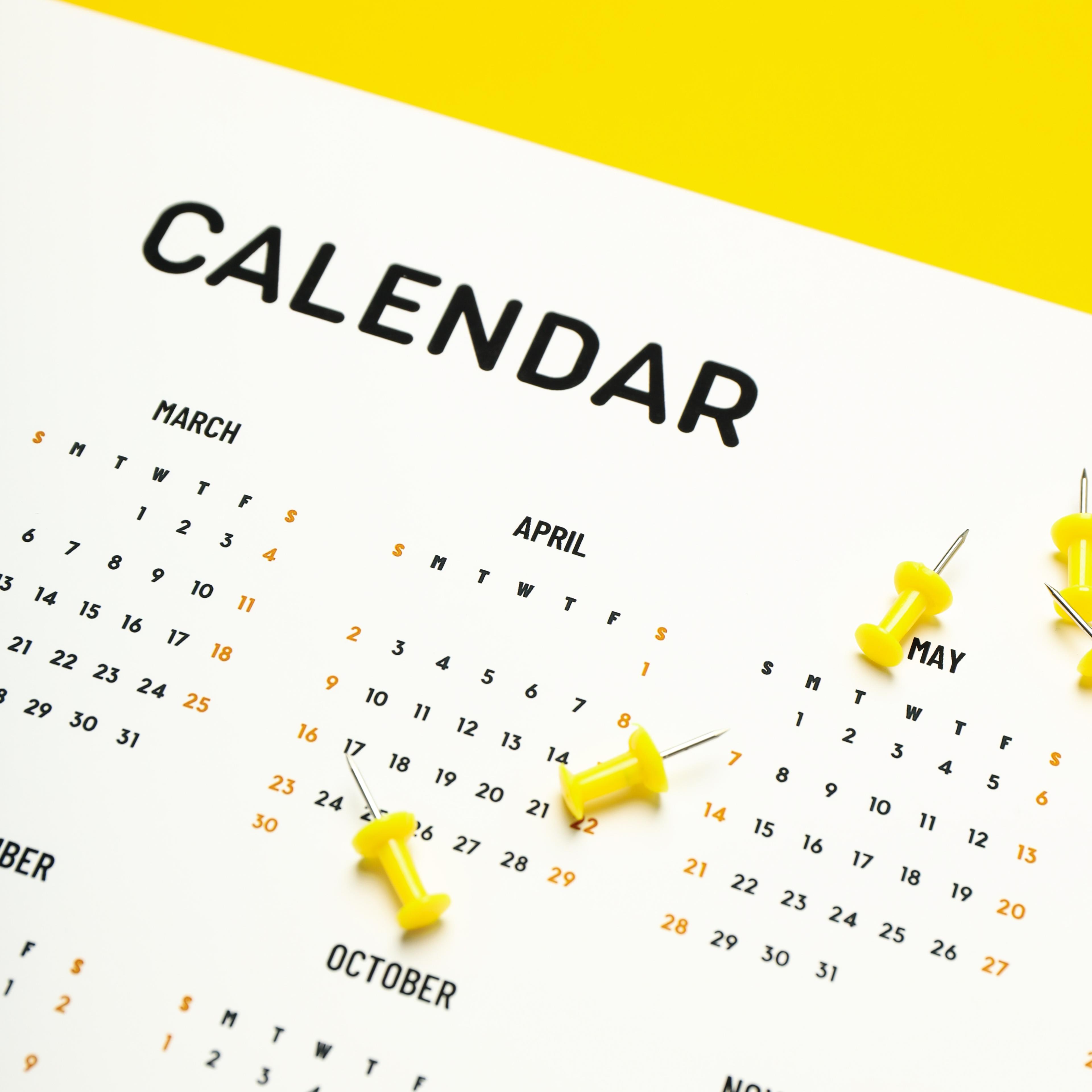 A calendar laying on a yellow table with yellow push pins on top of it.