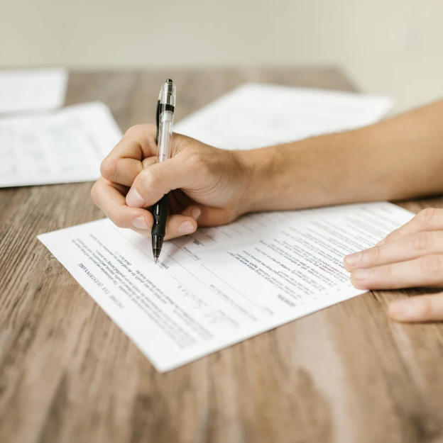 A hand filling out a form with a pen.