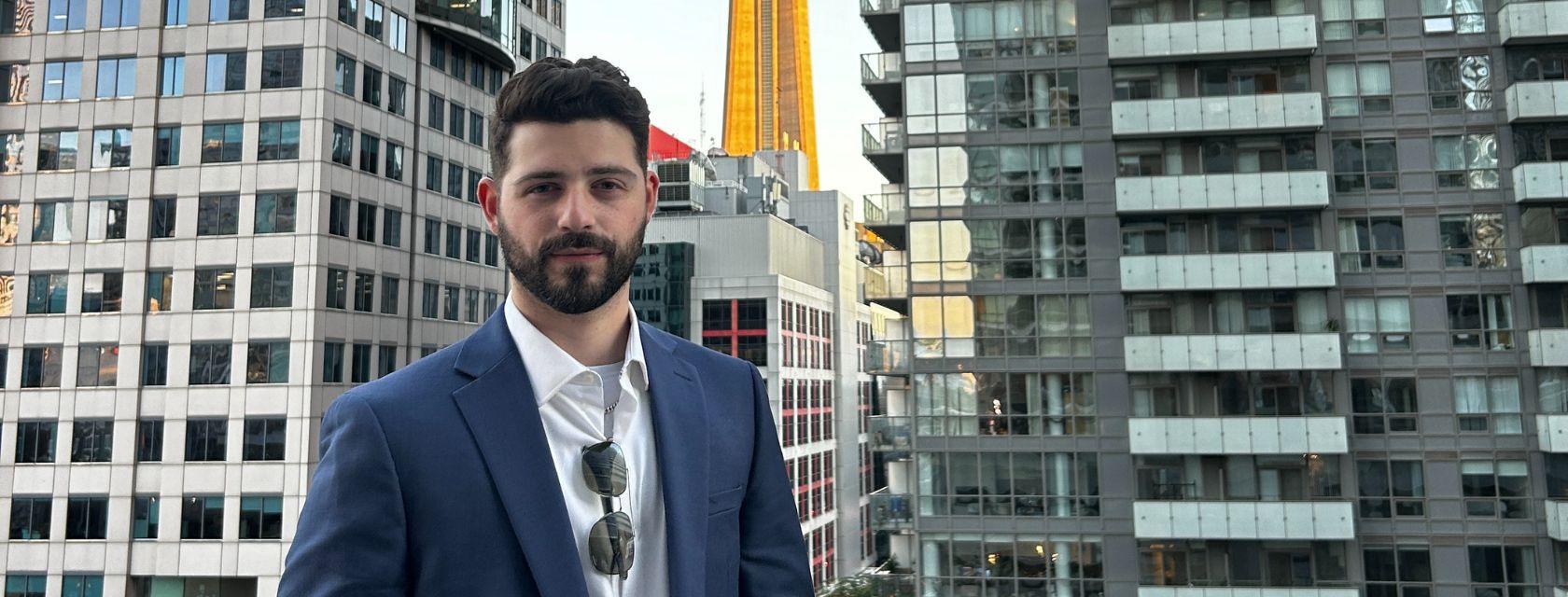 Matthew Hernandez stands in front of city skyline wearing a suit