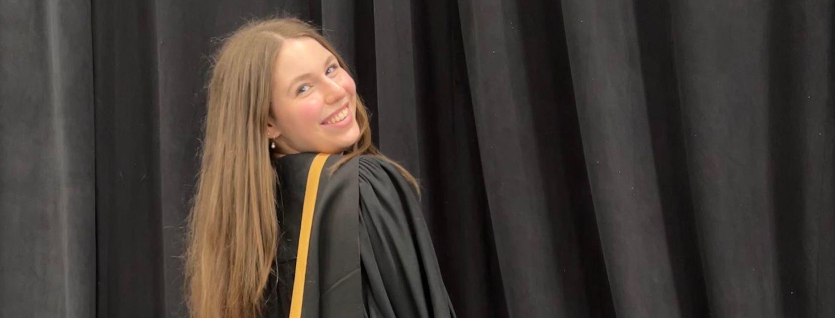 U of G Graduate wearing gown in front of a black backdrop.