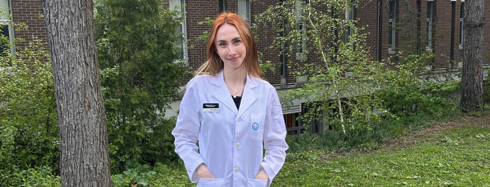 Grad student standing outside wearing a lab coat. 