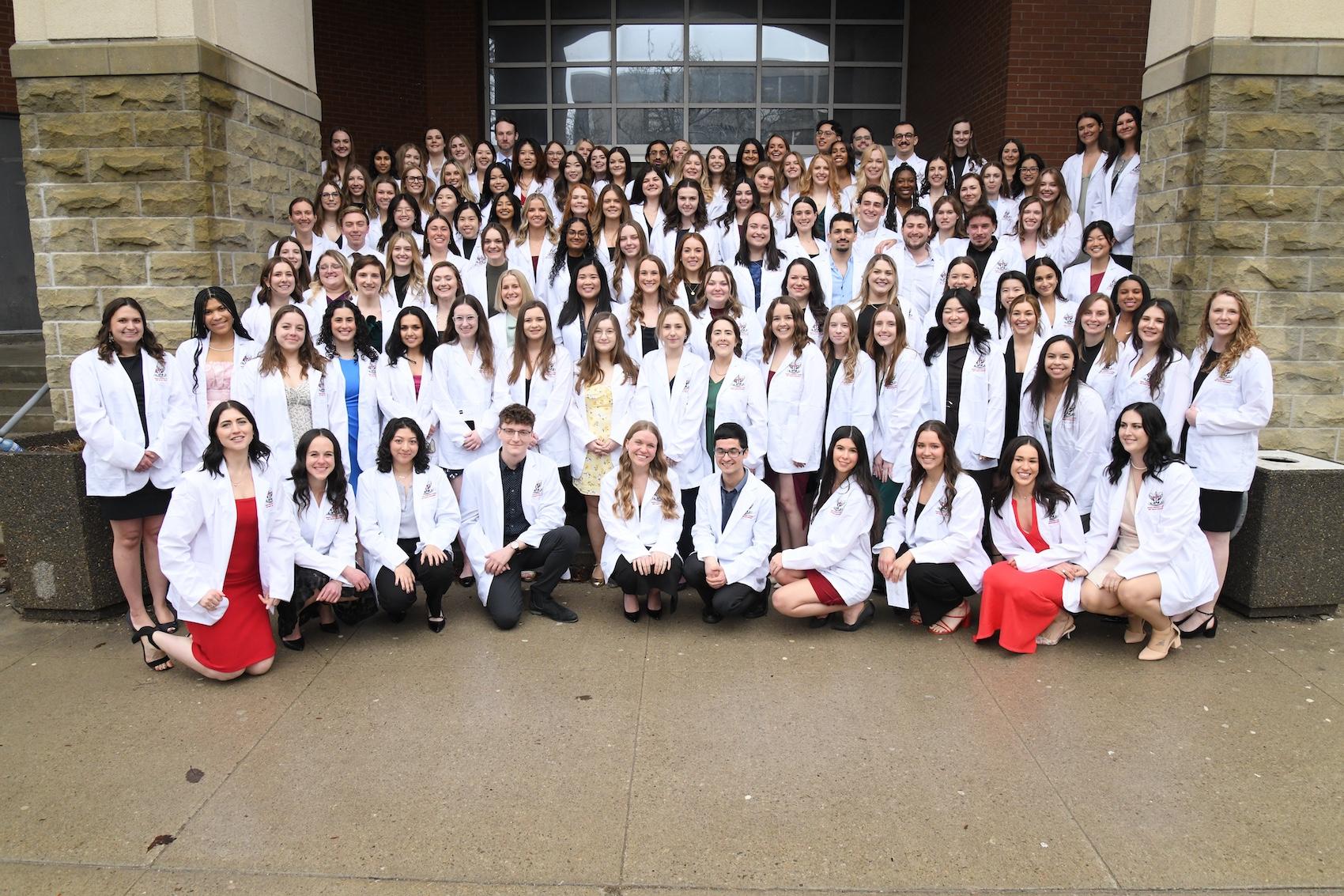 OVC class of 2026 wearing their white coats and posed on stairs of rozanski hall
