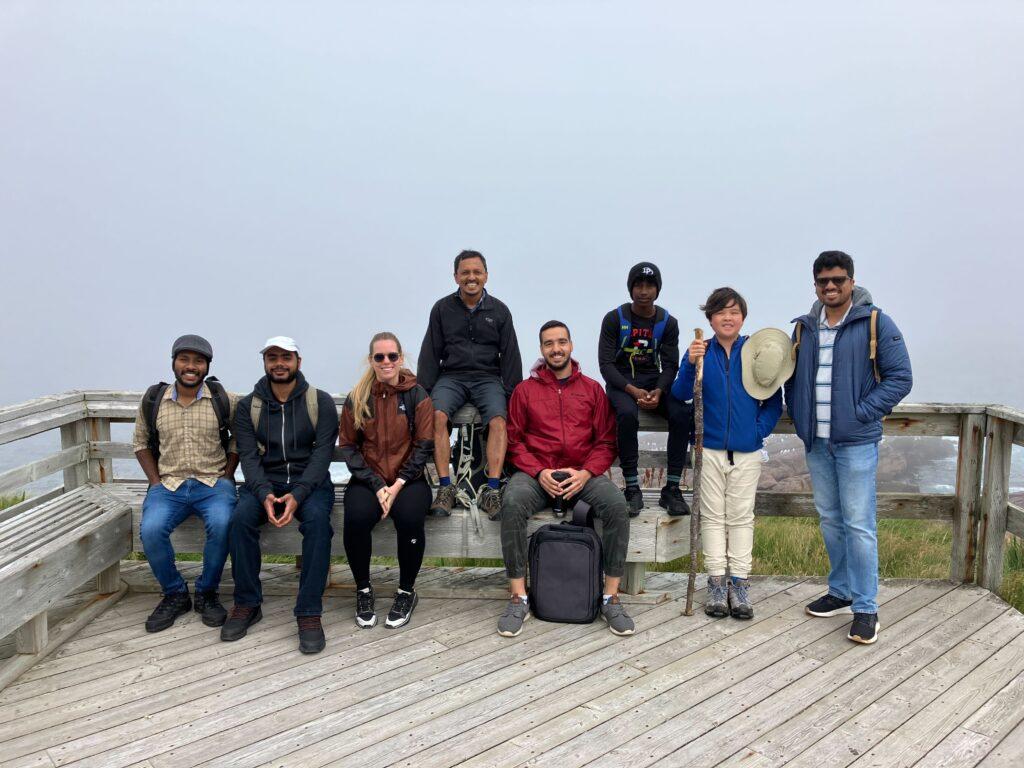 Group photo taken outdoors on a platform overlooking the ocean