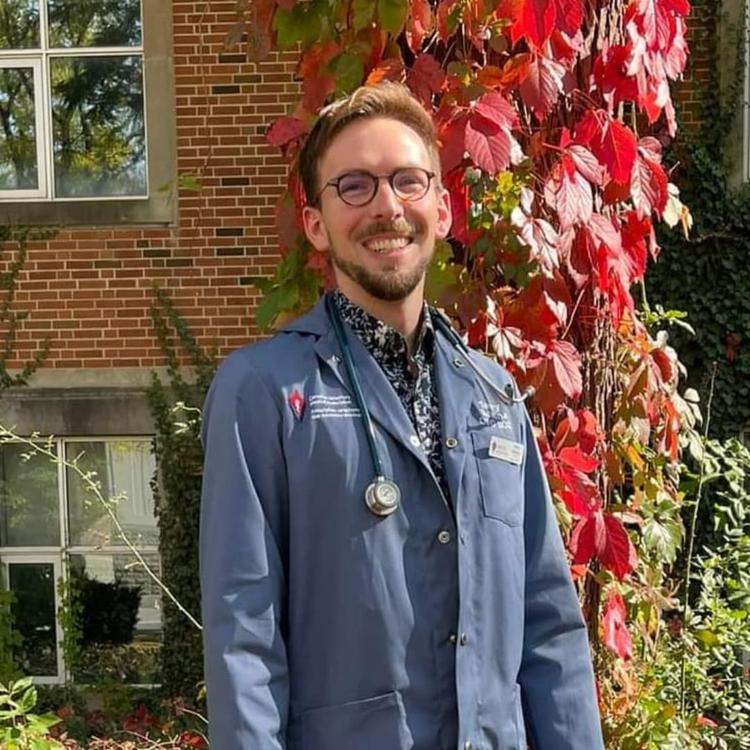 A man wearing a blue lab coat and a stethoscope around his neck