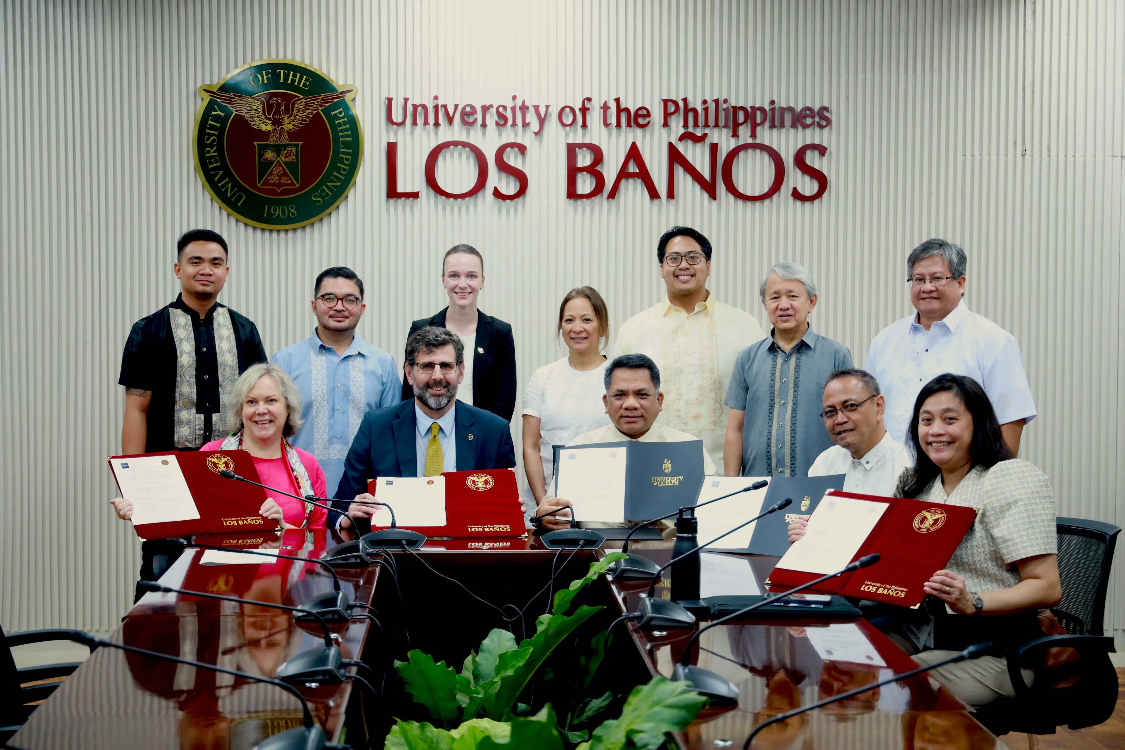 Staff from UPLB and U of G stand and sit, holding signed MoUs