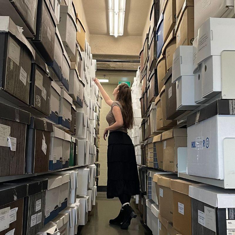 Grad Abigail Boorsma working in the archives among stacks of boxes.