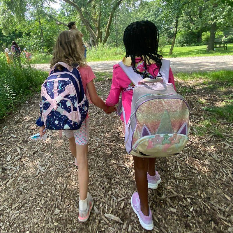 Two young Creative Encounters campers walking hand and hand through the Arboretum.