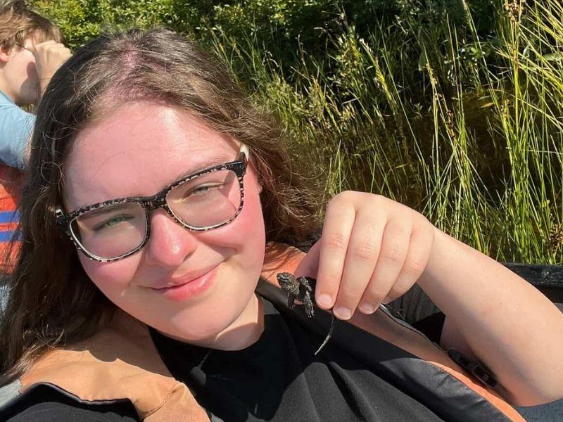 Heather smiles outside on a sunny day, while holding up a small turtle.