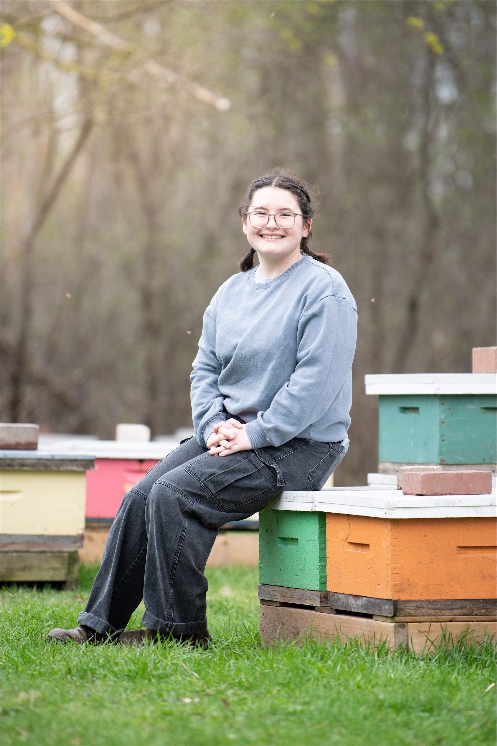 Laura sits outside on colourful wooden crates at a Honeybee Research Centre site.