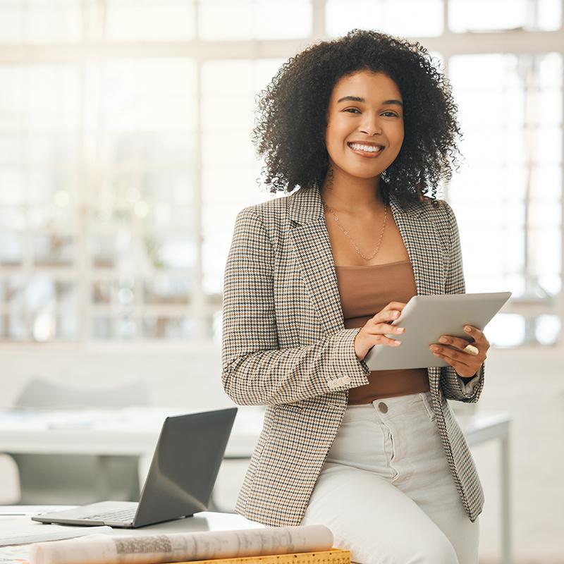 Professional woman sitting on the edge of her desk.