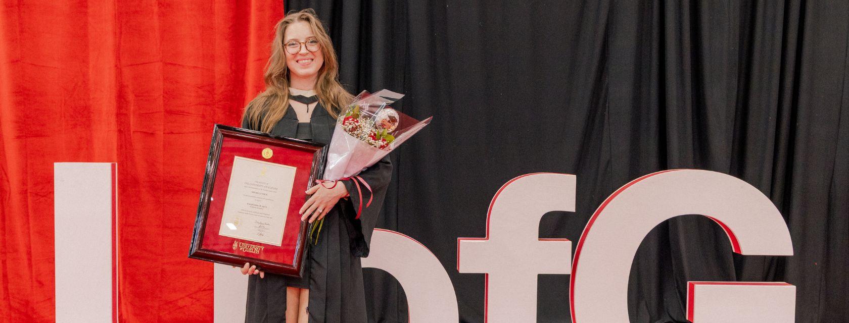 Justice and Legal Studies Grad Michelle Wilk posing in front of the U of G sign at her convocation. 