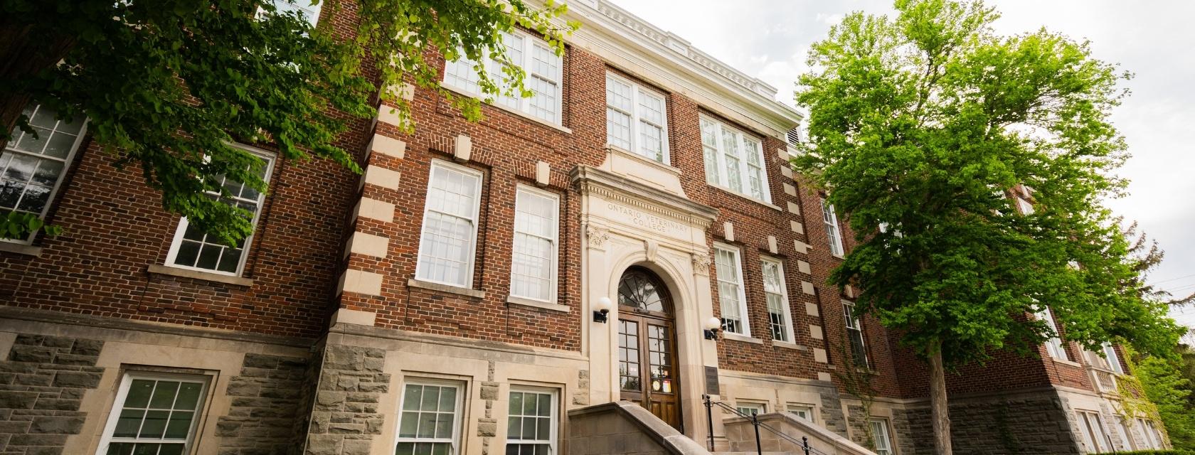 The front face of a red brick building with green trees around it