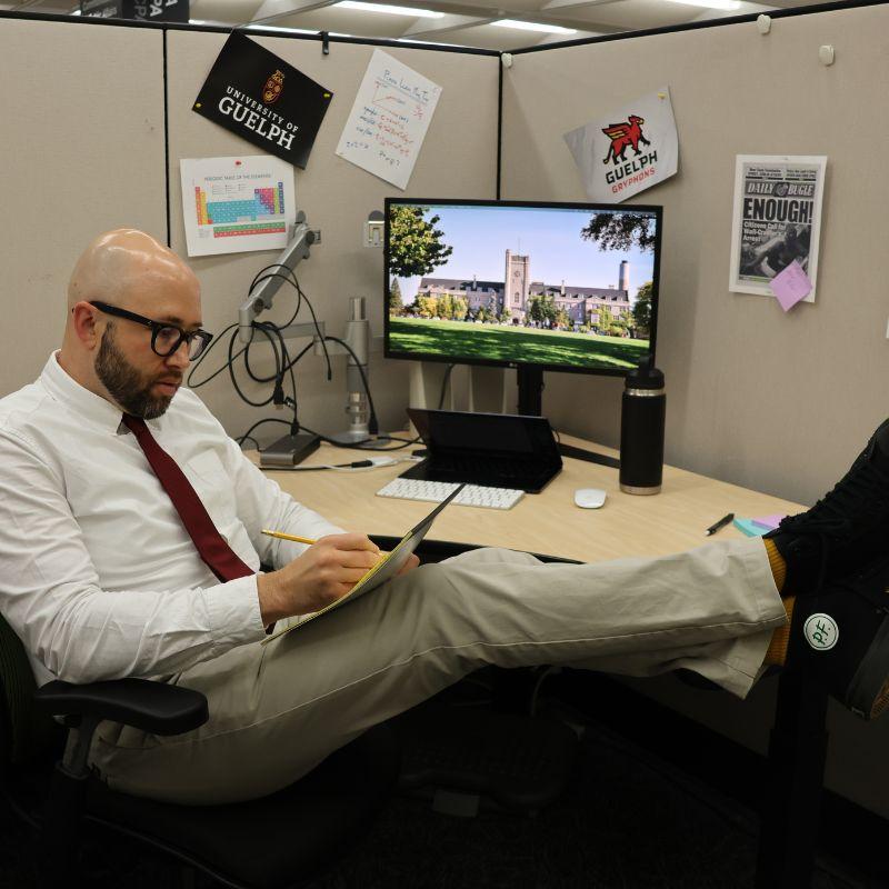 GradCast host sitting at his desk while writing on a pad of paper.