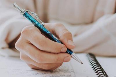 A person in a light pink shirt with a pen and a notebook