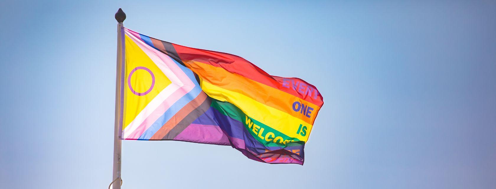 Pride flag flaps in the wind in front of a clear sky. 