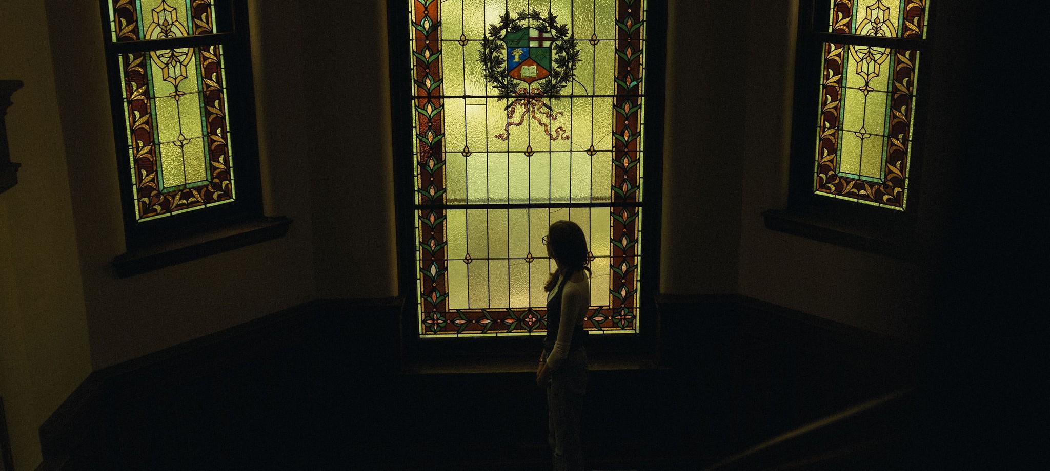 Student standing in front of stained glass windows at Massey Hall.