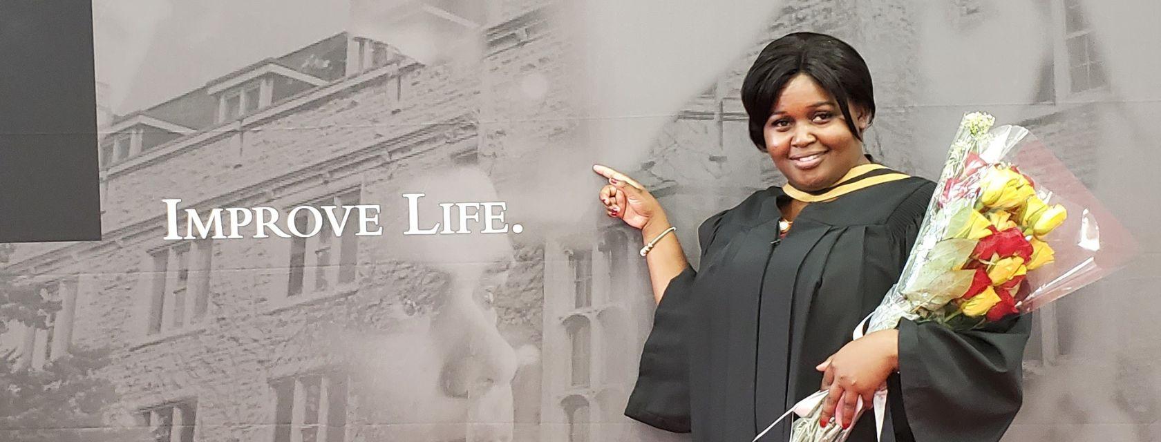 Beatrice Wausi Gedion poses in front of the Improve Life banner after completing her masters.