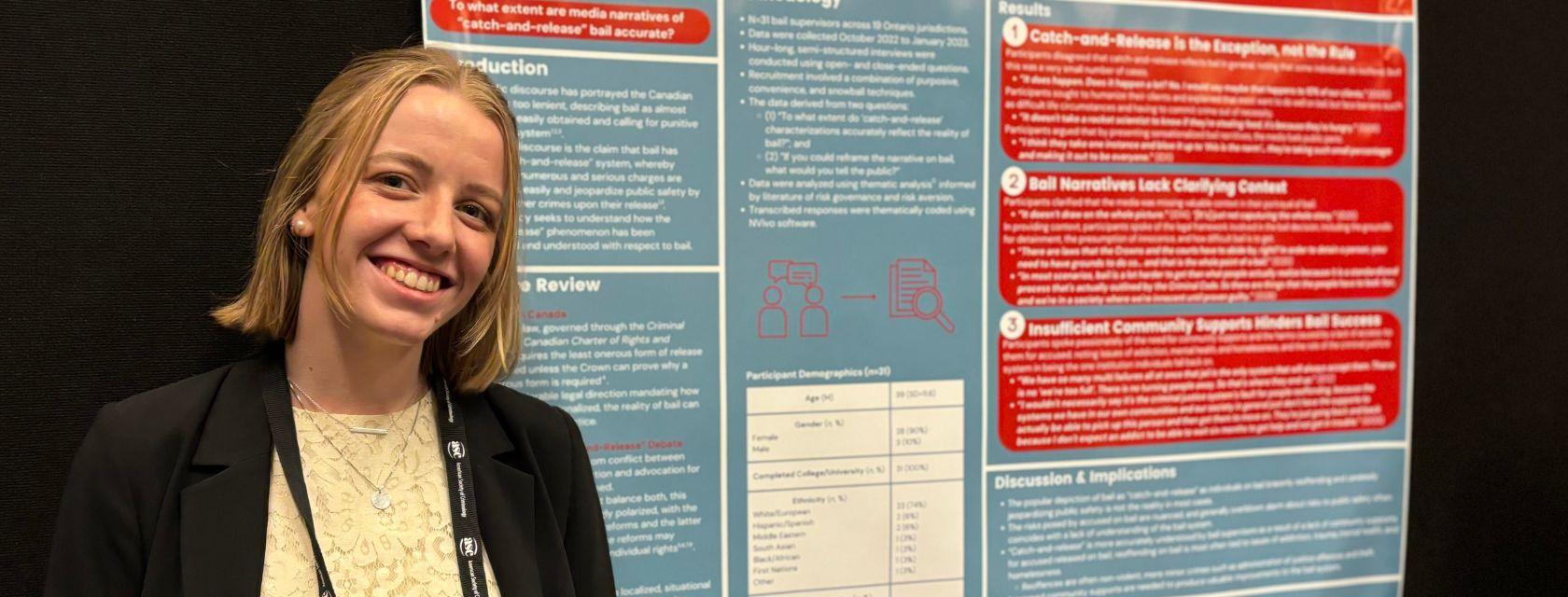 Guelph grad Alexandra Crowley wearing business casual clothing in stands in front of a large screen with text highlighting one of her projects. 