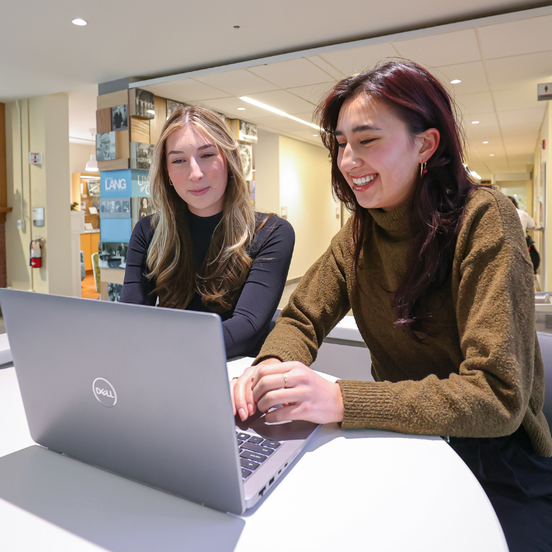 Two students smile while on a laptop together.
