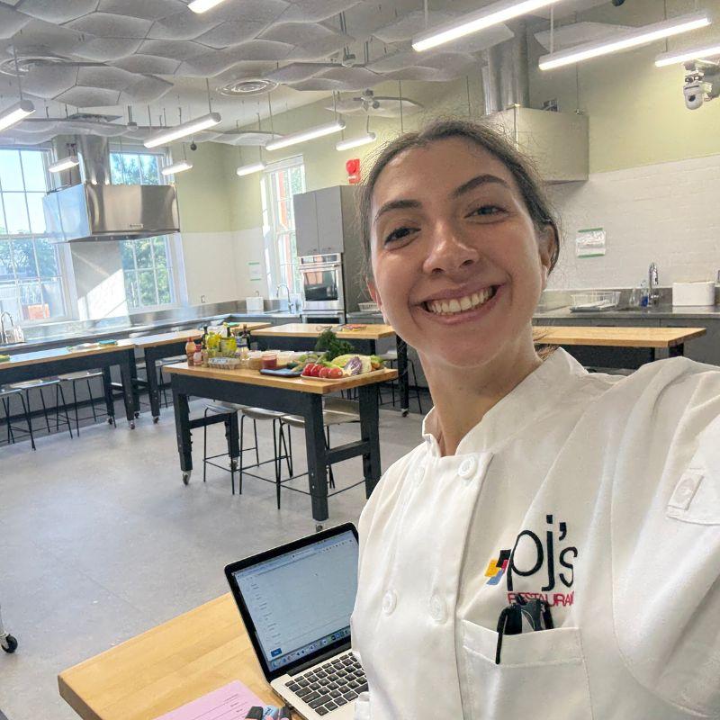 Applied Human Nutrition grad Paulina Morelli while wearing chef's whites. A prep kitchen can be seen in the background. 