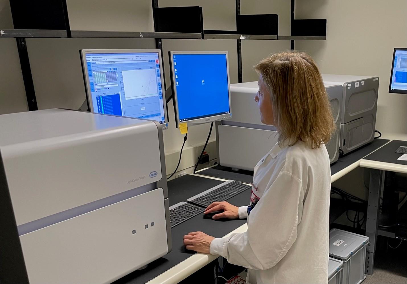 A lab coat wearing Animal Health Lab staff member checks one of two computer screens
