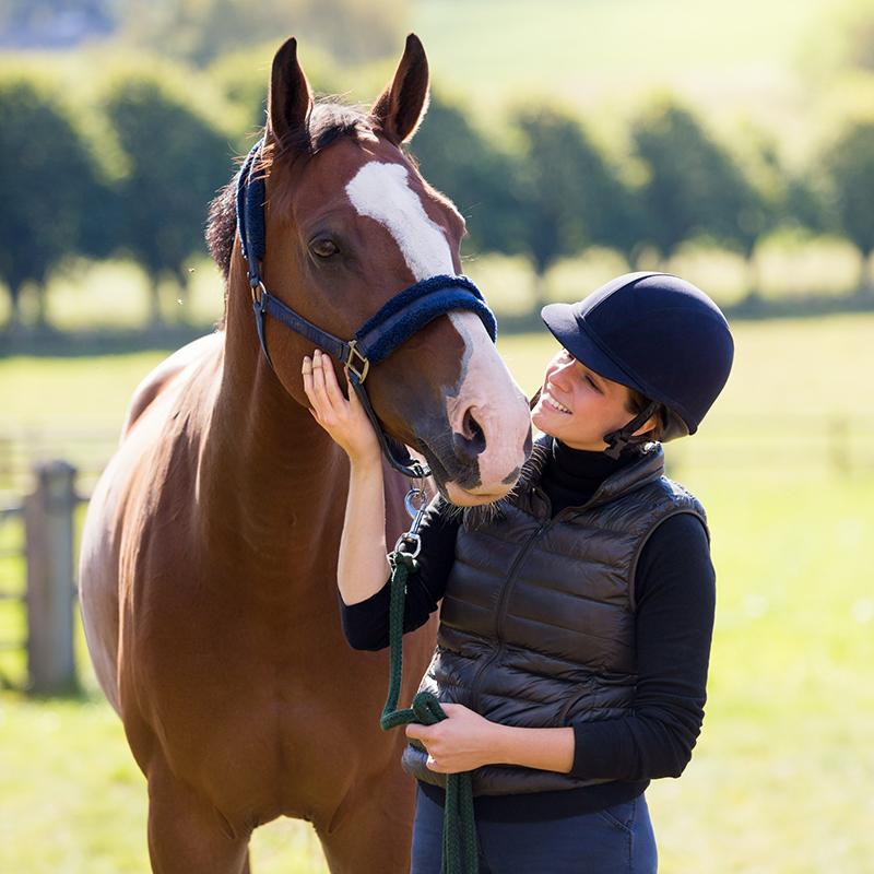 Woman with a helmet patting her horses head.