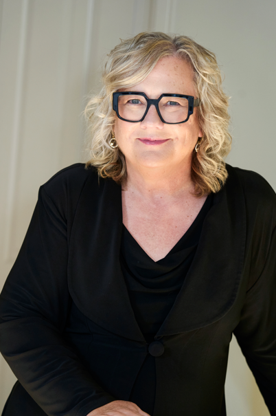 Headshot of Samantha Brennan, with blonde hair and black glasses.