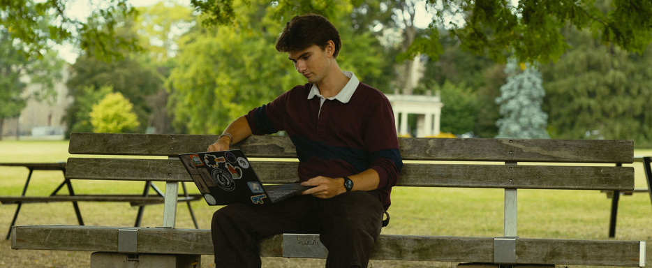 student sitting on bench on their laptop