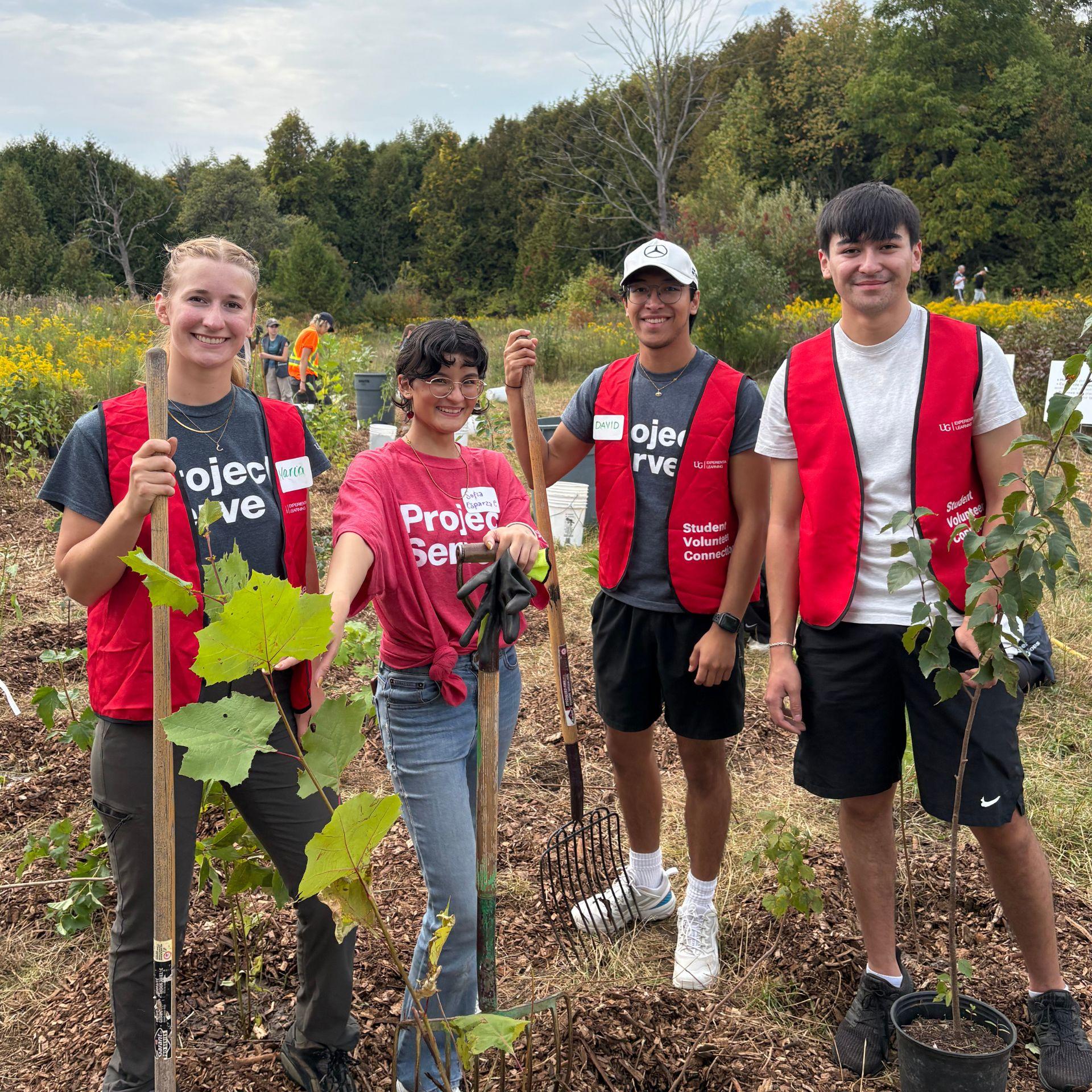 4 Project Serve volunteers stand holding shovels in a garden bed.