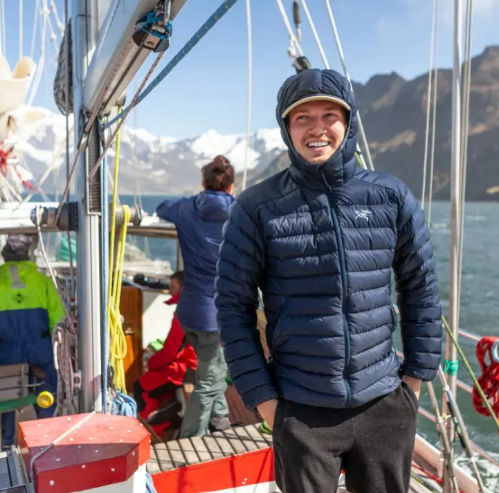 ryan standing on a boat with a blue winter jacket on, the hood is over his head