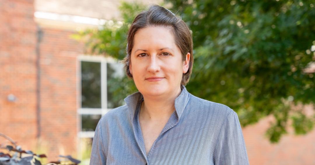 woman with brown hair and blue striped shirt standing with slight smile