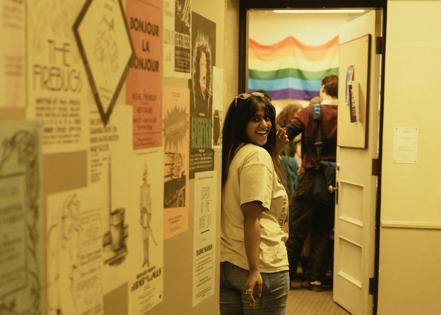 Student turning back looking and smiiling with posters and a pride flag around them