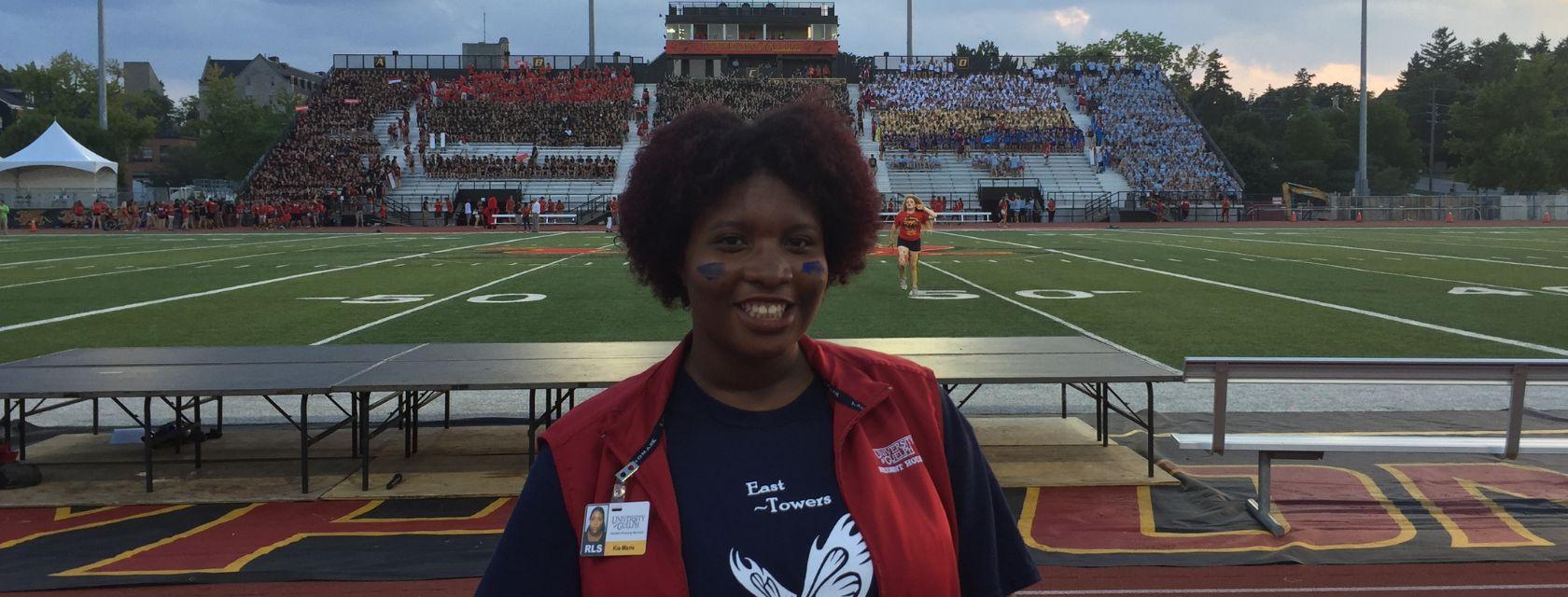 Guelph Grad Kia-Marie Parsons stands in front of a football field while wearing a red vest.