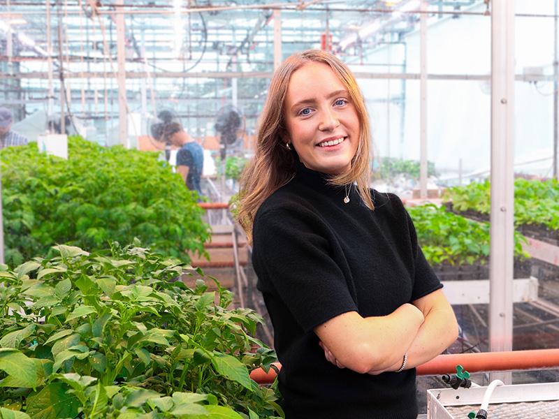 Peyton Nailor stands with her arms crossed in a greenhouse.