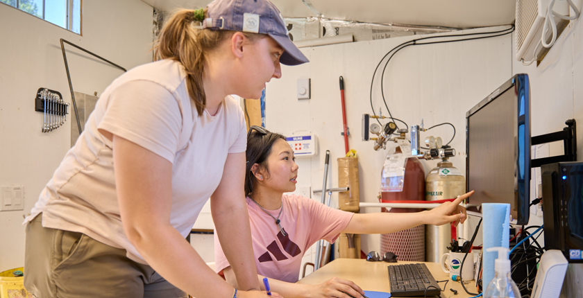 Chi Vi in the lab with a fellow student. Chi is pointing at something on a computer.