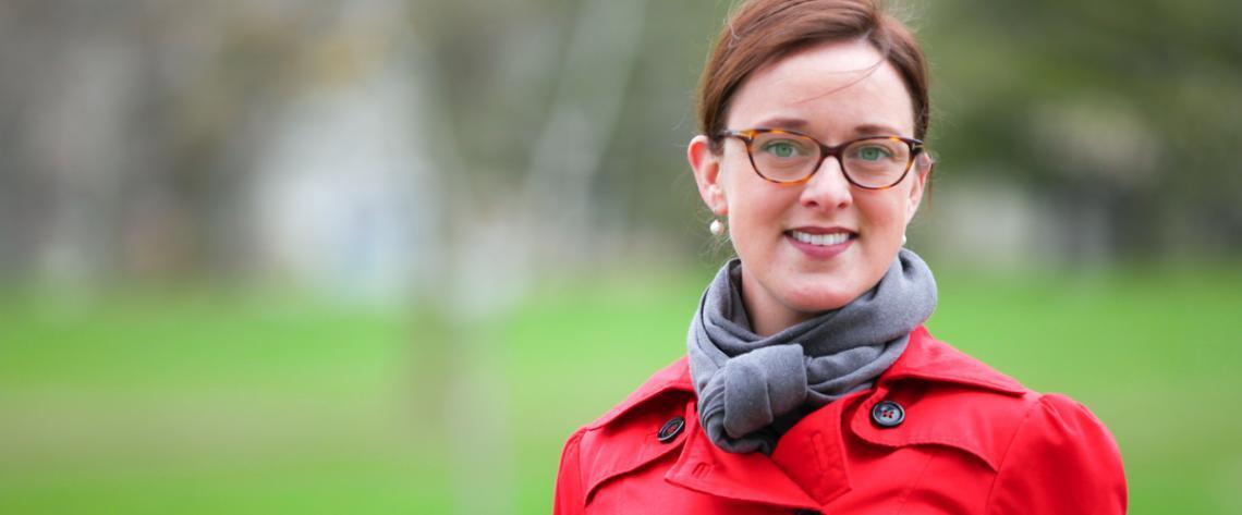 Dr Christine Baes in a red trench coat standing outside