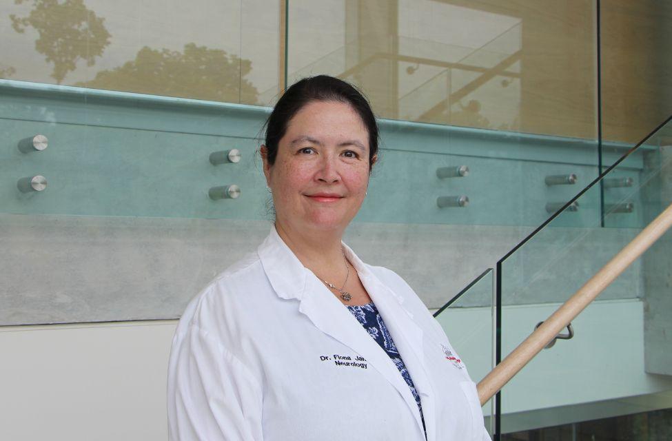 Dr. Fiona James poses in front of a glass wall while wearing a lab coat.