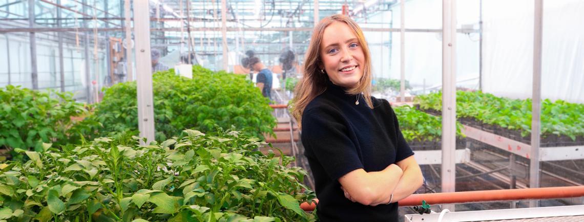 University of Guelph Student Peyton Nailor standing in a greenhouse surrounded by plants
