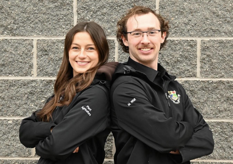 OACGSC Co-Directors, Julianna Tindall & Matthew Whitemore standing back to back with their arms crossed wearing matching black OAC jackets